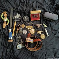 Top-down photo showing full lot on black fabric background including cufflinks, pocket watch, belt, shoe shine brush, figurines, and badges.