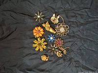 All 11 flower pins laid out on black cloth showing colors, designs, and sizes