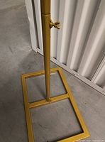 Close-up of the square base and lower part of one gold metal arch stand, showing adjustable wing nut clamp and gold finish