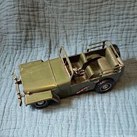 Side angled view of a green metal toy jeep showing two seats, steering wheel, and rear bench seat on a blue cloth.