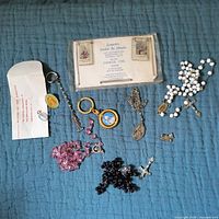 All items arranged on blue fabric background showing rosaries, keychains, and packaged scapulars