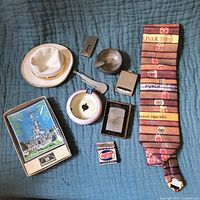 Overview photo showing the lot items including ashtrays, lighters, matchbox and cigar tie laid out on a blue quilted fabric.