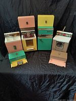 Full set of four vintage Barbie kitchen units including stove, refrigerator, sink, and dishwasher displayed on black backdrop.