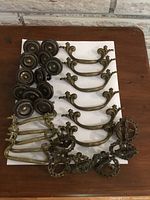 Overview of the antique brass drawer pulls showing round decorative pulls, curved handles, and ornate scrolled handles with wear and tarnish.