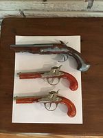 Top-down photo showing all three toy pistols on white paper.