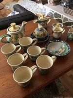 Photo showing full assortment of artisan pottery including teapot, mugs, creamer, sugar bowl and serving bowl on wooden table.