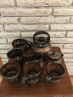 Full set of artisan pottery including teapot, cups, creamer, and sugar bowl arranged on wooden surface.