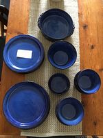 Top view showing various sizes of deep blue glazed ceramic plates and small and medium bowls arranged on a table runner.