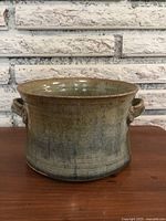 Front-facing image of blue-green glazed pottery pot with handles on both sides, showing its shape and glaze texture.