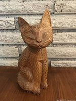 Front view of the wooden cat figure showing carved facial features, texture of fur, and sitting pose.