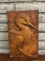 Front view of ceramic wall plaque showing detailed relief of a bird in warm brown tones.