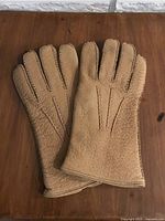 Top side view of tan leather gloves showing stitching details and texture.