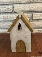 Front view of a small pottery church decoration with a cross on the peak, white walls and a brown roof