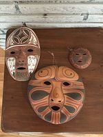 Three South Western pottery painted masks on a wooden surface, showing entire lot.