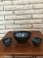 Photo showing enamelled metal bowl and two tea cups on a wooden surface against a white brick wall background.