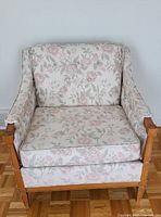 Front view of the 1960s traditional chair showing pink and cream floral upholstery and wooden legs and arms.