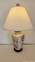 Full view of the ceramic floral design lamp with pleated cream lampshade illuminated, showing overall height, shape, and color tones.