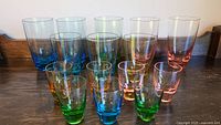Photo showing a total of 15 multicolor glass pieces arranged including highballs, shots, and tumblers.