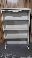 Front view of white wooden bookshelf hutch showing four shelves including a curved top shelf, straight legs and flat base, clean design with minor scratches
