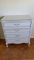 Front view of white dresser showing four drawers and gold trim.