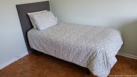 Twin bed fully assembled with grey fabric headboard, mattress, box spring, and bedding including duvet and pillows.