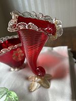 Red decorative glass bowl with clear leaf-shaped edges and feet, showing detail of clear leaf edges and curled foot