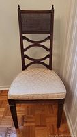 Front view of vintage wooden chair showing cream upholstered seat and caned upper backrest with decorative finials.
