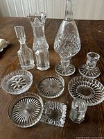 Photo showing full assortment of cut glass crystal items on wooden table including decanter, vase, oil and vinegar set, candlestick holders, salt and pepper set, and wine bottle holders.