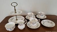 Full set displayed on table showing two-tiered cake plate, teacups, saucers, cream jug, and sugar bowl all with matching Royal Albert Brigadoon floral design and gold trim.