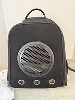 Front view of black backpack cat carrier showing circular vent and two small ventilation holes.