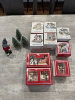 Overall lot laid out including five boxed village houses, boxed miniature carolers and sleigh scenes, a Swallings of Sweden figure, loose caroler figure, and four bottle brush trees.
