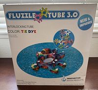 Box front showcasing product name Fluzzle Tube 3.0, tie dye color, dimensions 61x61 inches, new and improved, interlocking tube design.