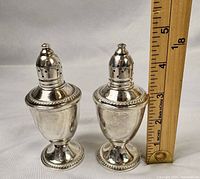 Pair of vintage sterling silver weighted salt and pepper shakers by Duchin Creations shown with measuring tape for scale, approximately 3.5" tall each.