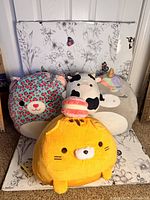 Photo of four plush toys including Chelsea the Cheetah, the cow, gray unicorn Squishmallow, and yellow cat with pink macaron.