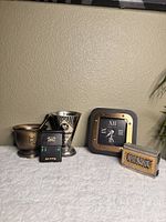 Brass mortar and pestle, Luchs Messbecher measuring cup, Mini Vegas Slots handheld electronic game, and Zodax Mark Lane desk clock set against beige wall