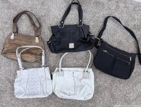 Lot of 5 purses arranged flat on carpet: 4 leather Tignanello purses in varying shades and styles, 1 black Travelon canvas purse with crossbody strap.