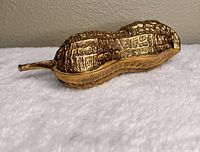 Photo showing brass peanut-shaped trinket box resting on white surface, showcasing the textured peanut shell detail.