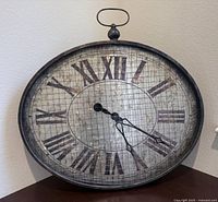 Front view of oval steampunk style large wall clock showing entire clock face, Roman numerals, and clock hands.