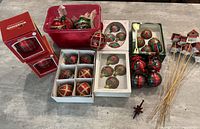 Several boxes and bins of tartan plaid Christmas ornaments in a variety of sizes and styles alongside decorative birdhouse sticks
