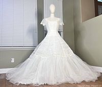 Front and full view of vintage 1950s white wedding dress on mannequin showing fitted bodice, lace short sleeves, and flared tulle layered skirt.