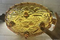 View of bottom of the oval amber carnival glass footed bowl showing raised harvest fruit pattern and four feet.