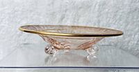 Side view of the pink depression glass compote dish showing the three footed base shaped like lilies and the gold trim around the rim.