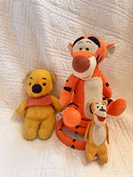 Three plush toys: yellow Winnie the Pooh, large orange Tigger, and small orange corduroy Tigger.