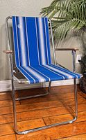 Side angle view of the vintage Zip Dee folding lawn chair showing blue striped fabric and metal frame with wooden armrests.