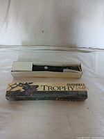 Rifle scope visible inside a white insert tray within original Bushnell Trophy 3-9x40 box with elk graphic and some box damage.