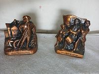 Front view showing both copper-tone Centennial Banks with detailed patriotic scenes and inscriptions.