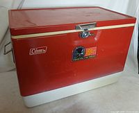 Front side of the red and white vintage Coleman ice chest showing latch lock and stickers