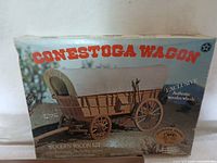 Box of Conestoga Wagon wooden model kit featuring image of finished wagon model with authentic wooden wheels on the cover.