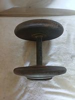 Full view of an adjustable metal dumbbell with round weight plates on both ends and a straight handle in the center. The dumbbell shows surface rust and wear.