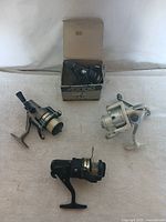 Four fishing spinning reels arranged on a surface, including one reel inside its original box.